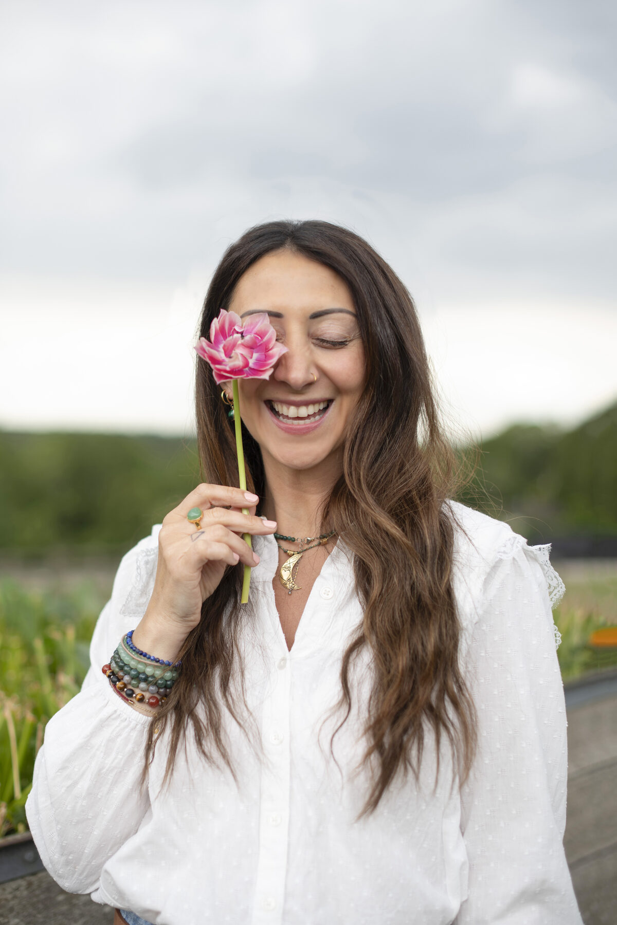 Lauren Vaknine smiling, holding a pink flower in front of one eye