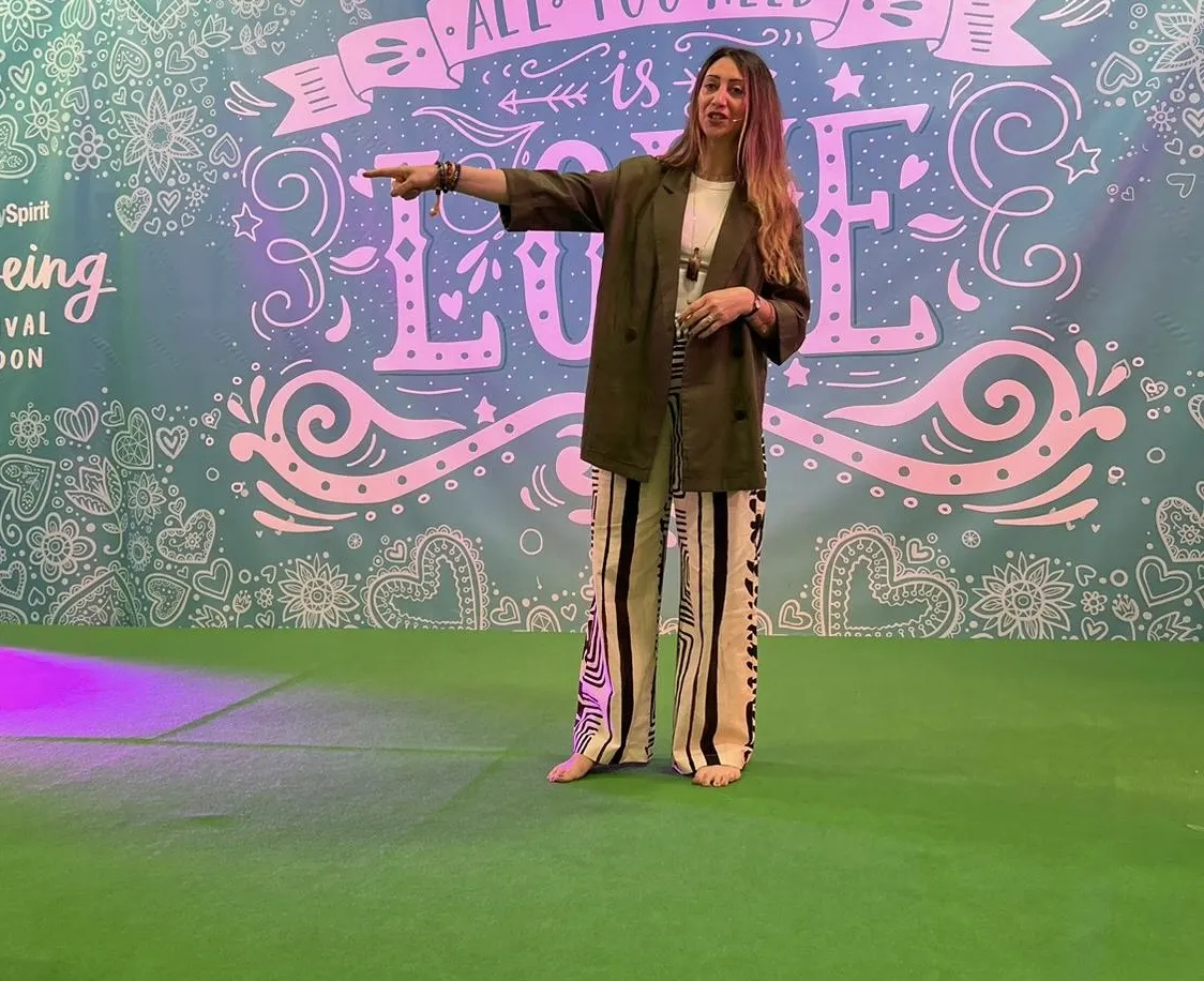 Lauren Vaknine speaking on a stage in front of a large "All you need is love" mural
